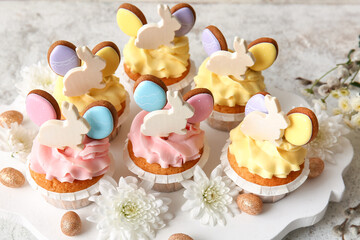 Board with tasty Easter cupcakes, eggs and flowers on light background, closeup