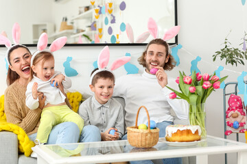 Obraz na płótnie Canvas Happy family in bunny ears with Easter eggs sitting on sofa at home