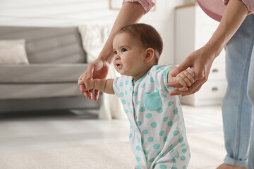 Mother supporting her baby daughter while she learning to walk at home