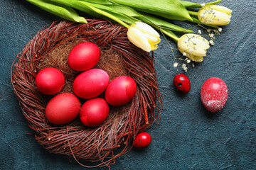 Nest with red painted Easter eggs and flowers on dark background