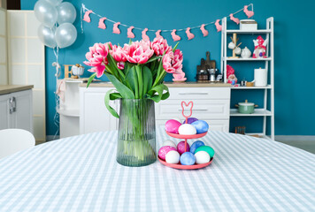 Stand with Easter eggs and vase with tulips on dining table