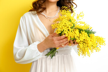 Beautiful young woman with mimosa flowers on yellow and white background