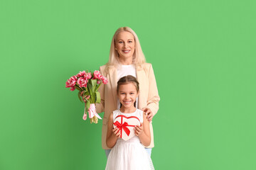 Mature woman with her little granddaughter and gifts on green background. International Women's Day