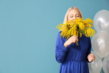 Mature woman with mimosa flowers and balloons on blue background. International Women's Day