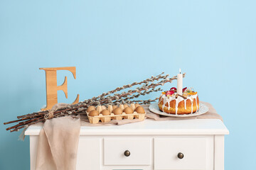 Holder with eggs, Easter cake and pussy willow branches on table near color wall