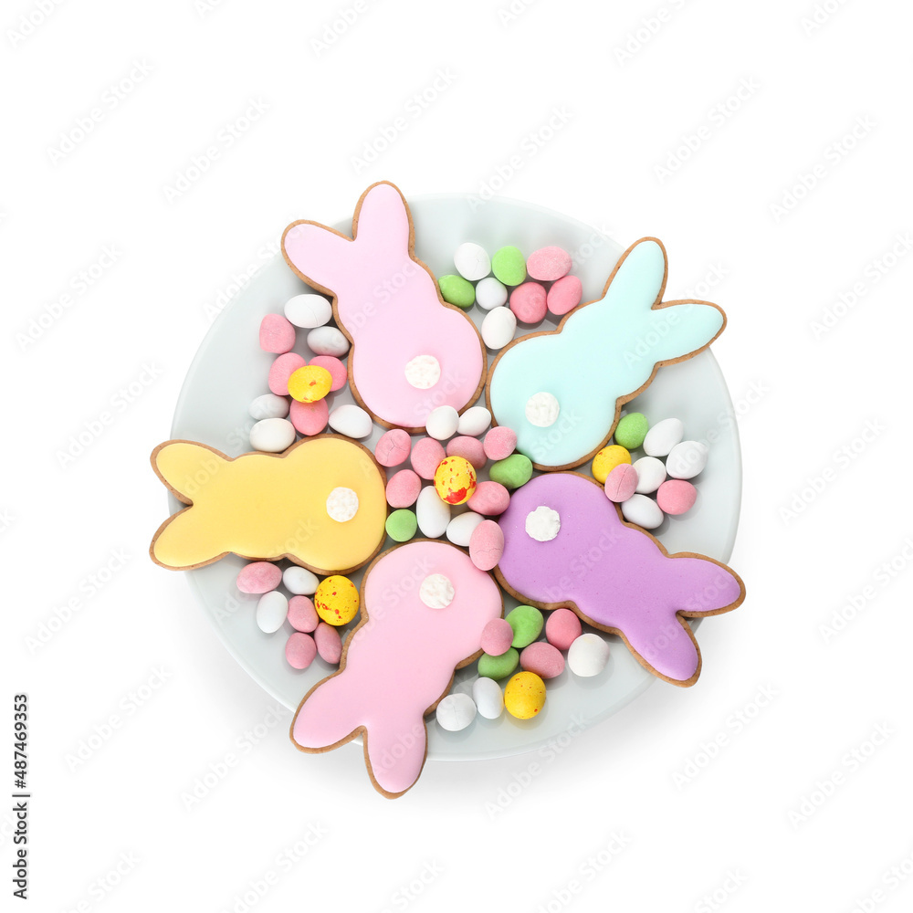 Wall mural Plate with delicious Easter cookies in shape of bunny and candies on white background