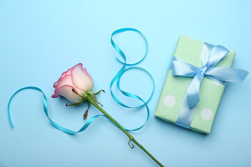 Figure 8 made of ribbon, gift box and flower for International Women's Day celebration on blue background