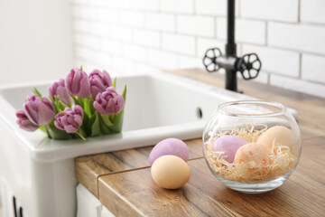 Fototapeta na wymiar Easter eggs and sink with tulips on kitchen counter near white brick wall