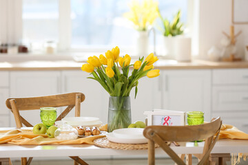 Dining table with setting and beautiful tulips in light kitchen. International Women's Day celebration