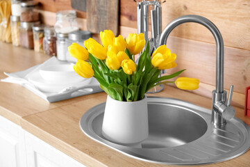 Vase with tulips in sink near wooden wall
