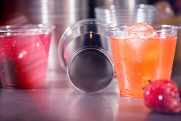 Clear plastic cups with red yellow and orange juice drinks splashing from ice cube on white background
