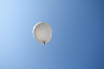 picture of white balloon flying under clear blue sky and sunlight on left