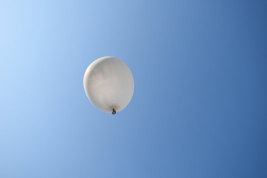 picture of white balloon flying under clear blue sky and sunlight on left