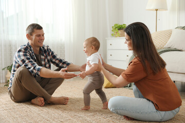 Parents supporting their baby daughter while she learning to walk at home