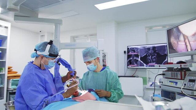 Surgeon puts device with camera into patient’s nose. Chief doctor looks at operation process on the screen in front of him.
