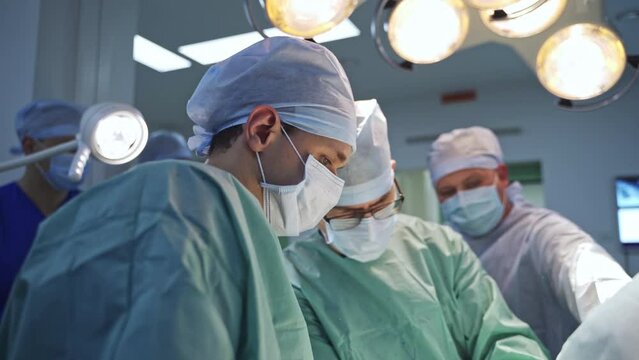 Multiple doctors team conducting operation. Male surgeons standing under the lights at modern operational theatre. Medical care concept.