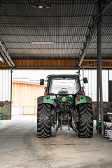 Modern green good-looking tractor stands in outside garage near agricultural fixtures and transport...