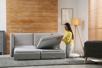 Young woman unfolding sofa into a bed in room. Modern interior - Powered by Adobe