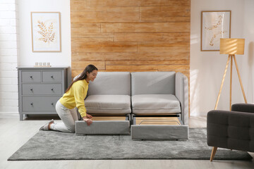 Young woman unfolding sofa into a bed in room. Modern interior - Powered by Adobe