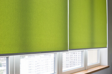 Roller blinds closeup on the window in the interior. Roller shades for big windows. Electric curtains for office. Green color, monochrome material. Window coverings. - obrazy, fototapety, plakaty