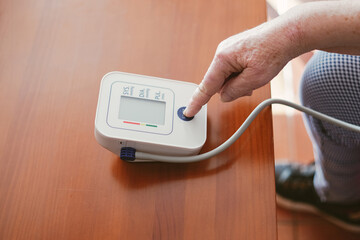 old woman presses the start button of a blood pressure monitor with her finger - obrazy, fototapety, plakaty