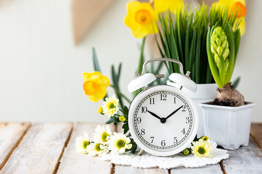 Spring change, Daylight Saving Time concept. White alarm clock and flowers on the wooden table