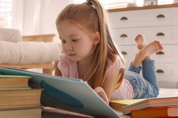 Fototapeta na wymiar Cute little girl reading book on floor at home
