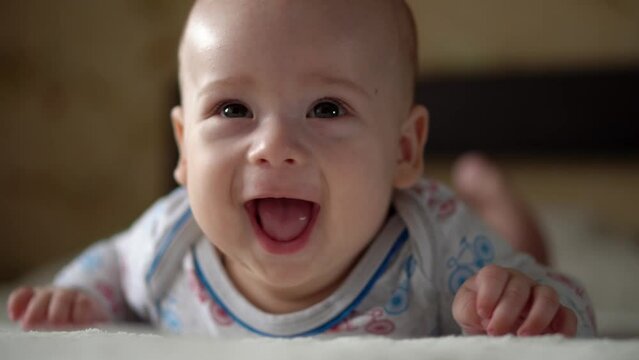 Newborn Active Baby Cute Smiling Teethless Face Portrait Early Days On Stomach Developing Neck Control. 5 Months Child On White Bed Looking on Camera. Infant, Childbirth, Parenthood, Beginning Concept