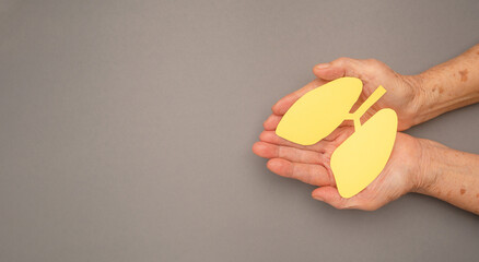 Lungs shape made from yellow paper on a palm old woman on a gray background