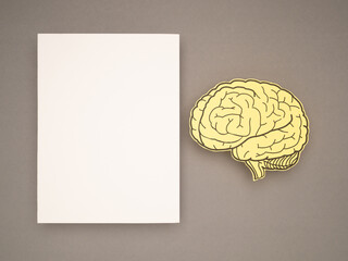 Blank white paper and a brain shape made from yellow paper on a gray background