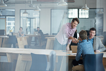 Welcome to the team. Through the glass shot of a group of colleagues working together in an office.