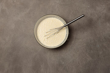 Obraz na płótnie Canvas A bowl of batter and a whisk for whipping. Top view on a gray background.