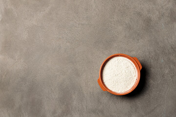A bowl with flour or white powder on a gray background. Top view on a gray background, a copy of the space
