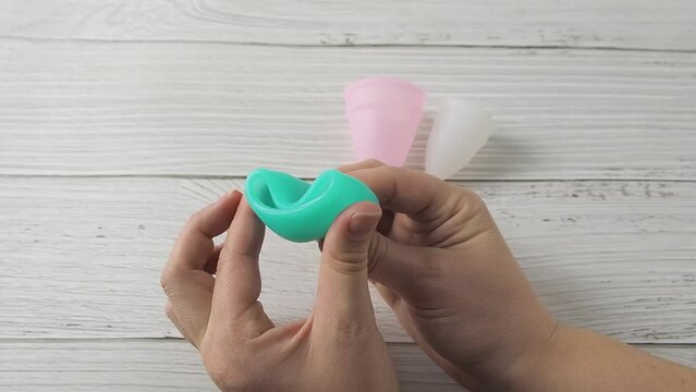 Woman hand holding different types menstrual cups and demonstrating Punch Down folding methods. Intimate menstruation hygiene period. Zero waste alternative medical silicone products