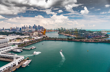 The huge busiest logistic port in Singapore, plenty of cranes to move containers, huge cargo ships in the background, shopping malls and skyscrapers surrounded by, entertainment island nearby