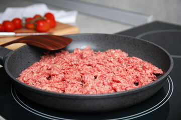 Frying pan with raw minced meat on induction stove, closeup
