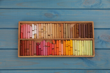 Drawing pastel set in box on light blue wooden background, top view
