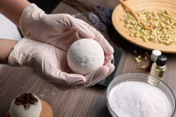 Woman holding handmade bath bomb above wooden table, closeup