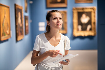 Portrait of young female visitor with paper guide at paintings exposition