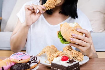 Fotobehang Binge eating disorder concept with woman eating fast food burger, fired chicken , donuts and desserts © doucefleur