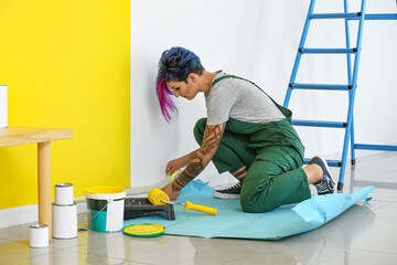 Female decorator with tape preparing wall for painting in room
