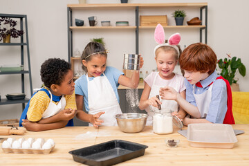 Children wearing apron browsing Internet on digital tablet in order to find recipe of appetizing cookie