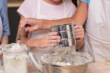 Cute little girl wearing apron passing ripe tomato to elder sister while cooking delicious salad together, kitchen interior on background