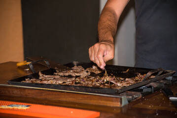 hand placing spices on meat cooked on iron griddle