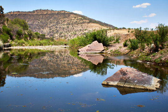 paisaje de la selva baja caducifolia con monta&ntilde;as aridas y un lago en primer plano rocas grandes al rededor y un cielo azul con nubes vida en un rancho de monte escobedo zacatecas 