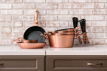 Set of different kitchen utensils on counter near light brick wall