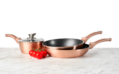 Copper saucepan with frying pans and tomatoes on table against white background