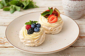 Plate of tasty Pavlova cakes with fresh berries on light wooden table