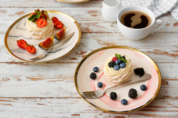 Plates of tasty Pavlova cakes with berries on light wooden background