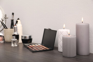 Mirror, candles and different makeup products on dark wooden dressing table near wall